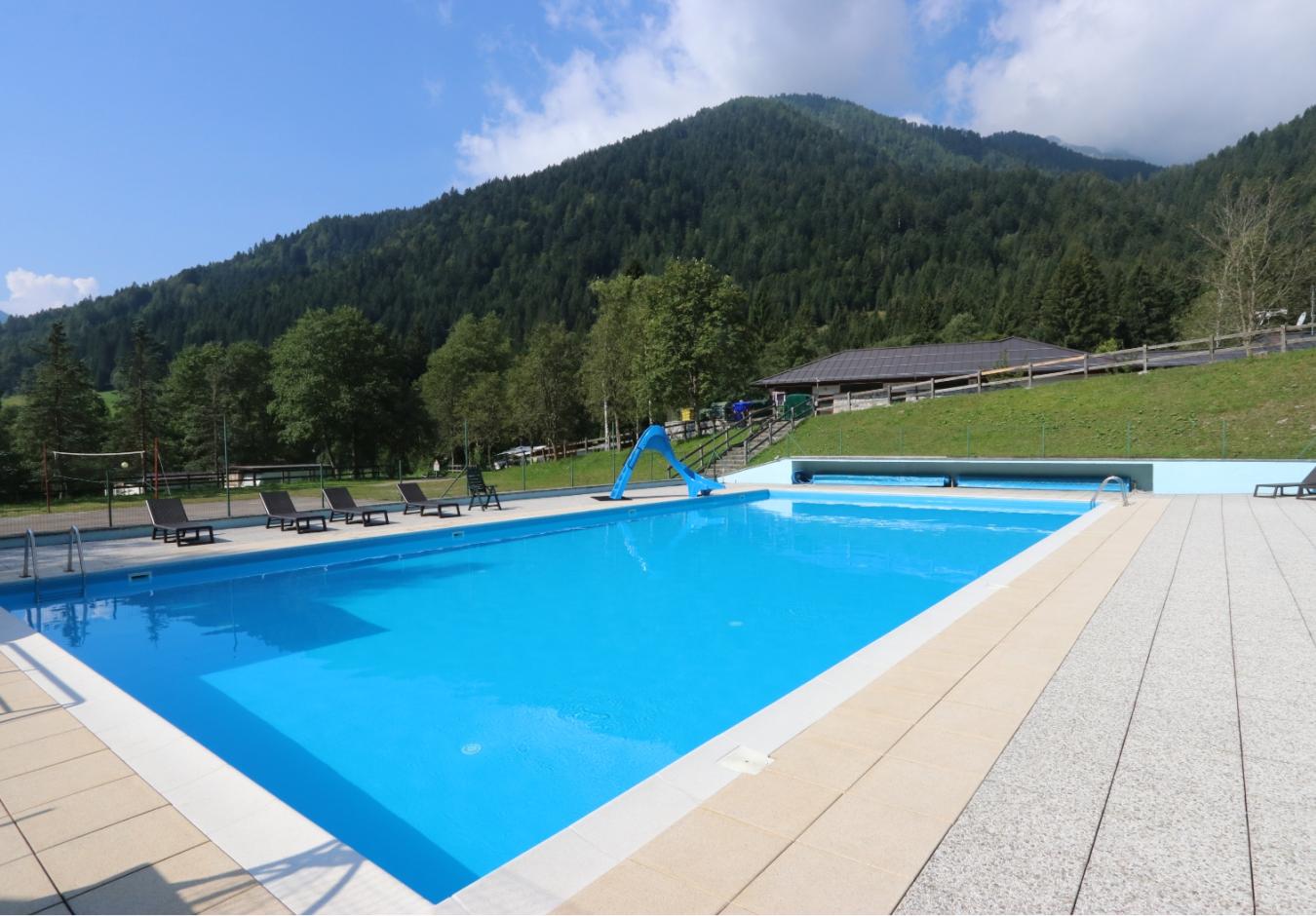 Piscina all'aperto con scivolo, circondata da montagne e lettini.