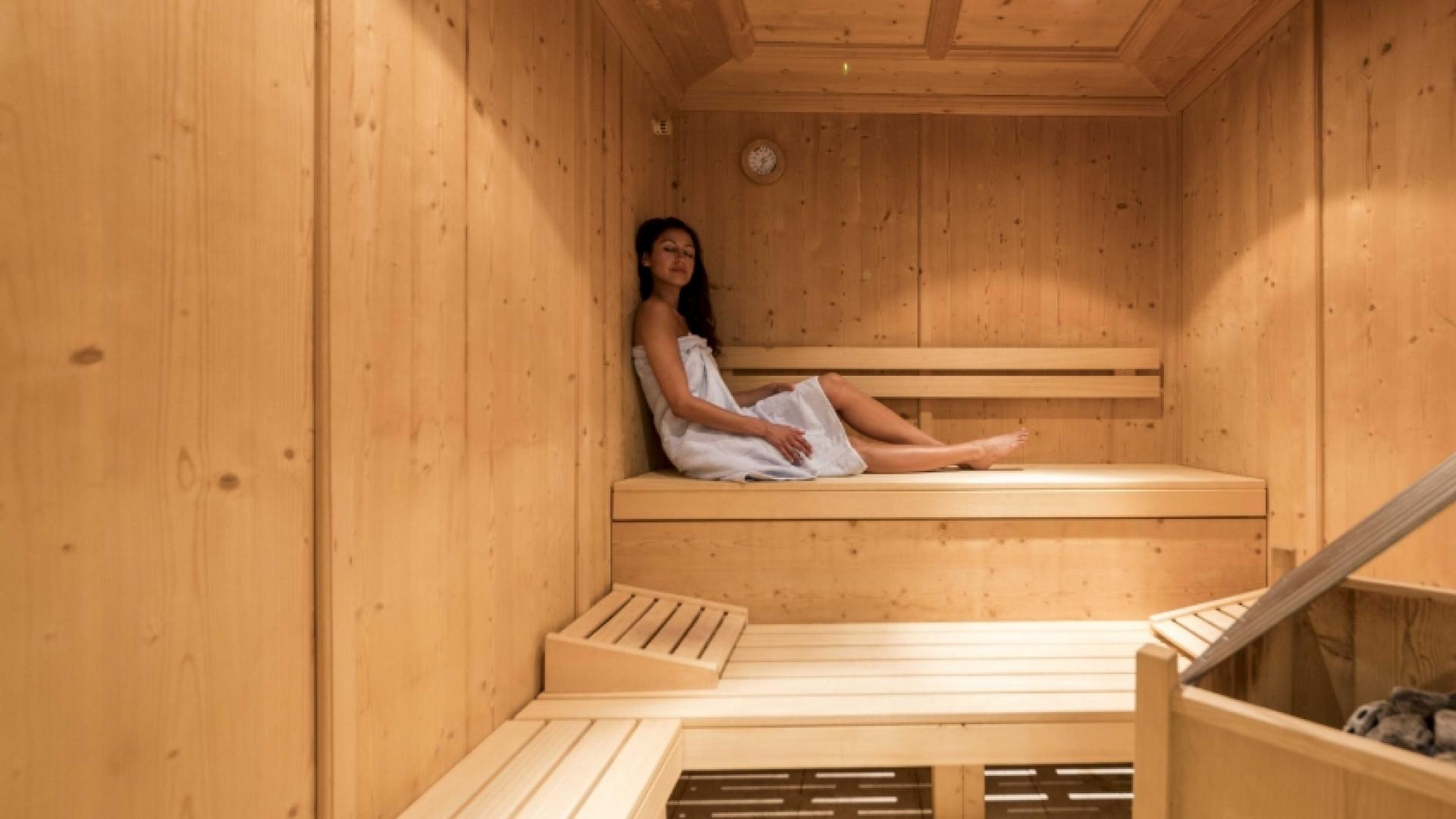 Donna rilassata in sauna di legno, avvolta in un asciugamano bianco.