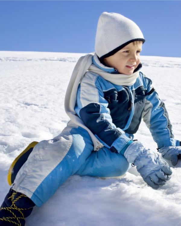 Bambino con tuta da neve e cappello bianco gioca sulla neve.