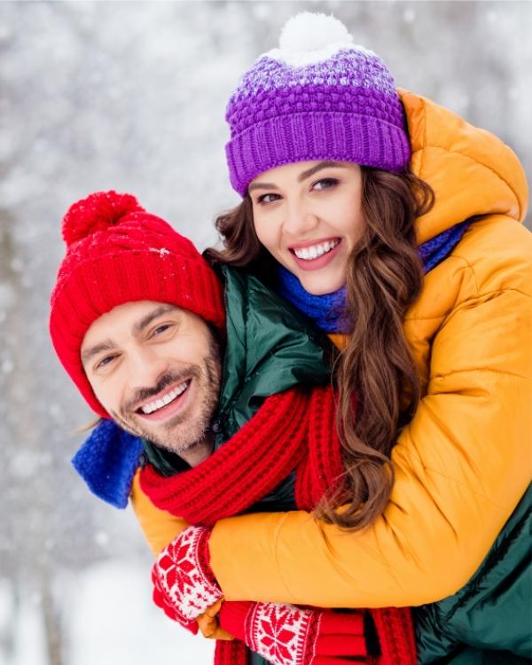 Coppia sorridente in abiti invernali colorati, abbracciati nella neve.