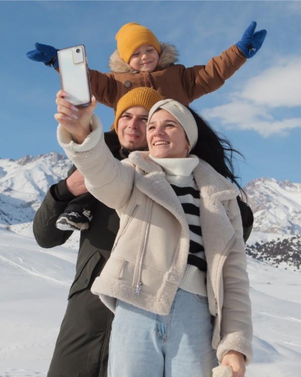 Famiglia felice scatta un selfie sulla neve con montagne sullo sfondo.